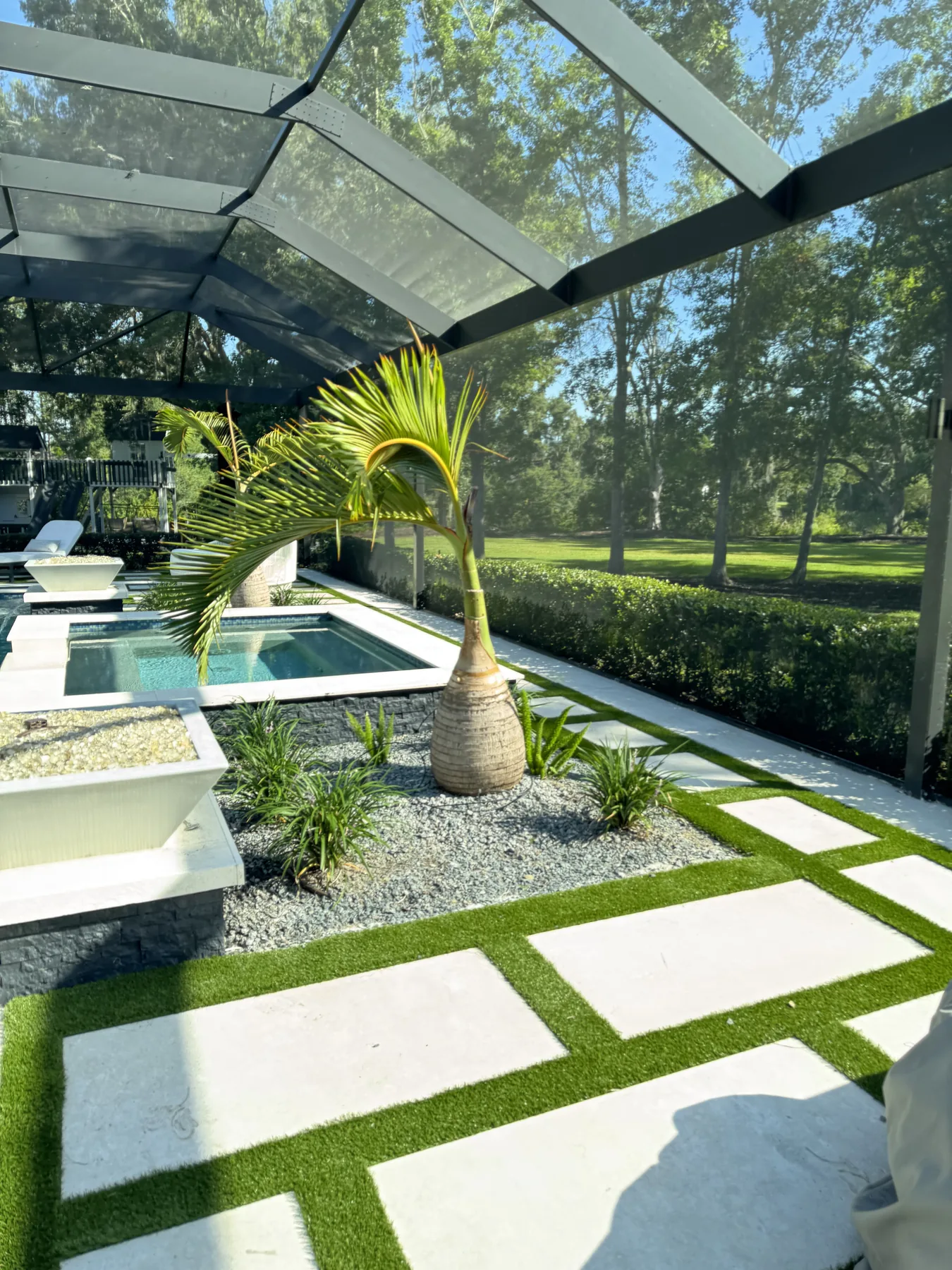 Modern pool courtyard with palms, stone, and geometric turf